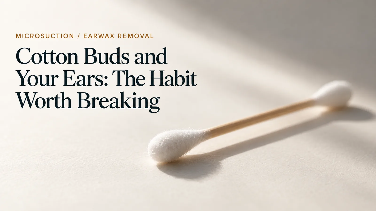 A single cotton bud resting on a pale surface in soft, low light.